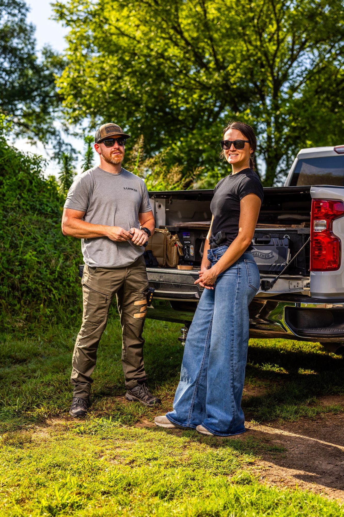 Smiling woman wearing a Clinger holster beside a man at a pickup truck outdoors